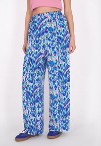 Luftige, blau gemusterte Hosen mit einem bunten abstrakten Druck. Elastischer Taillenbund und leichter Stoff, kombiniert mit blauen Turnschuhen.