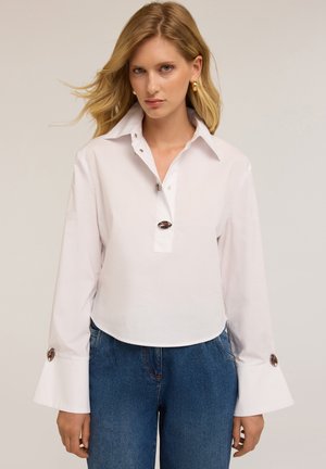 Witte katoenen shirt met een puntkraag, lange klokmouwen, een knopenlijst met drie knopen en decoratieve knoopaccenten op de manchet.