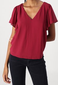 Bordeaux blouse van lichtgewicht stof, met korte, gerimpelde mouwen en een V-halslijn. Gecombineerd met donker corduroy broek.
