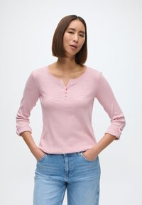 Φωτεινό ροζ μακρυμάνικο πουκάμισο με ριγέ υφή, διαθέτει V-λαιμό και τέσσερις κουμπιά. Συνδυάζεται με μπλε τζιν.