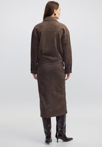 Bruine suede jas gecombineerd met een bijpassende lange rok, met een eenvoudig ontwerp en gladde textuur. Draag met kniehoge, donkerbruine laarzen.