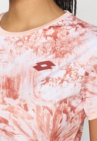 Αθλητικό μπλουζάκι κοντό μανίκι από μαλακό, απορροφητικό ύφασμα. Διαθέτει αφηρημένο σχέδιο σε ροζ και κοραλλί, με κοντράσ�τ σκούρα λογότυπο.
