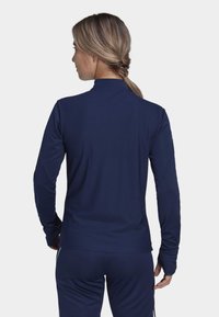 Navyblaues langärmeliges Sportoberteil mit strukturiertem Design, hohem Kragen und Daumenlöchern an den Bündchen. Dehnbare Stoff für Komfort.