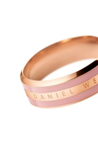 Bracciale in oro rosa con strisce alternate di smalto rosa e metallo lucido. Inciso "DANIEL WELLINGTON" su una fascia metallica. Texture liscia e lucida.