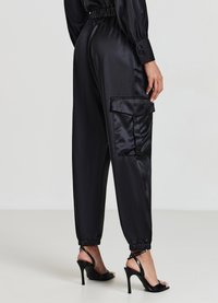 Pantaloni cargo neri in satin con una vestibilità comoda, caviglie elasticizzate e tasche laterali; abbinati a sandali neri con tacco.