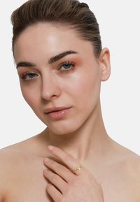 Bague en or avec un design de croix, présentant une bande lisse et polie ainsi qu'une texture délicate. L'arrière-plan est neutre et discret.