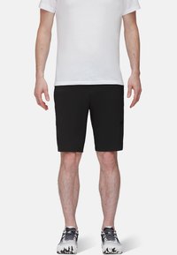 Pantalones cortos deportivos negros confeccionados en material ligero, con un diseño de corte recto y dobladillo cosido. Llevados con una camiseta blanca básica y zapatillas con un diseño estampado.