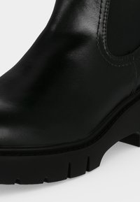Bottine en cuir noir avec panneau latéral élastique, bout arrondi et semelle crantée épaisse avec petit talon.