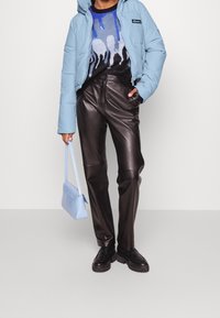 Jasnoniebieska, pikowana kurtka; czarny sweter z niebieskim wzorem w krople; czarne skórzane spodnie; jasnoniebieska torebka; masywne czarne buty.