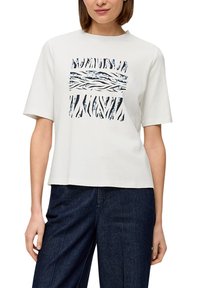 Biała bawełniana koszulka z krótkim, prostokątnym fasonem, z niebieskim i czarnym abstrakcyjnym wzorem na środku. Krótkie rękawy i okrągły dekolt.