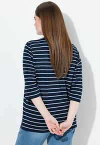 Tummansininen ja vaaleansininen raidallinen paita, jossa on kolme neljäsosaa hihat, rento istuvuus, sivurei'ät helmassa, yhdistettynä vaaleisiin farkkuihin.