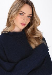 Marineblaues Strickpullover mit strukturierter Oberfläche und hohem, geripptem Kragen. Weicher, lässiger Schnitt mit sichtbaren Fasern und langen Ärmeln.