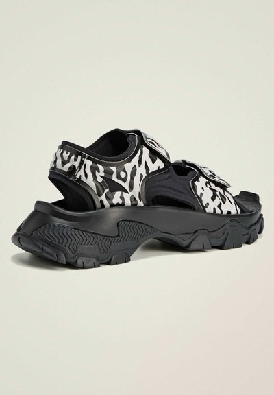 Zwart-wit gemusterde sandalen met een chunky zool, voorzien van verstelbare banden en een verstevigde hiel voor ondersteuning en duurzaamheid.