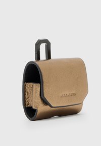 Mała metaliczna brązowa skórzana saszetka z czarnymi wykończeniami, z klapką zakrywającą i czarną geometryczną rączką na jednolitym tle.