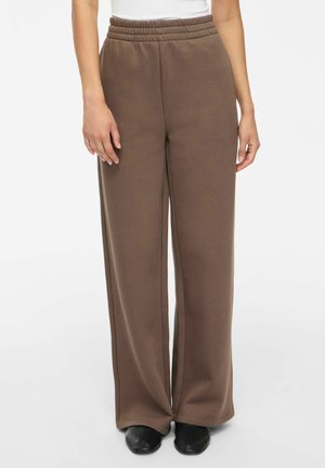 Pantalon marron à jambes larges avec taille élastique porté avec des chaussures noires et un haut blanc, visible de la taille aux pieds.