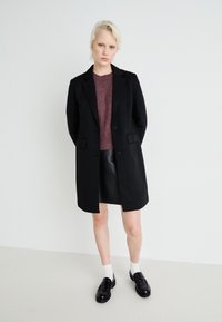 Čierny kabát z vlnenej zmesi s klopami a dvoma prednými vreckami, nosený cez vínový sveter a čiernu koženú sukňu, doplnený o šnurovacie topánky.