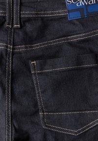 Mörka jeans med en slät yta, framträdande gula sömmar, och en enda bakficka. Har en blå märk på midjebandet.