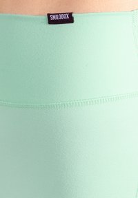 Leggings vert menthe en tissu lisse et extensible avec une ceinture plate. Comprend une étiquette logo noire et des détails de coutures discrètes.