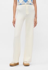 Široke hlače iz kremaste pletene tkanine, z gumbom za zapiranje in teksturiranim zaključkom. V kombinaciji s bež platformami.