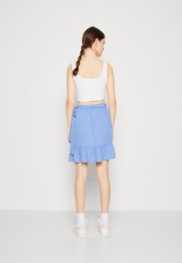 Jupe bleu à pois avec un ourlet froncé et un lien à la taille, associée à un haut court blanc et des baskets blanches.