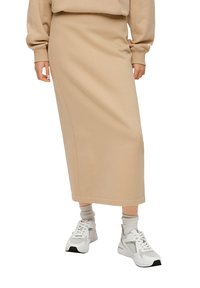 Beige midi rok van zachte stof, met een recht gesneden ontwerp en subtiele zijnaaddetails. Gepaard met witte sneakers en grijze sokken.