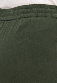 Tejido ligero de color verde oscuro con una superficie ligeramente texturizada y una cintura elástica. Caída suave y ajuste relajado.