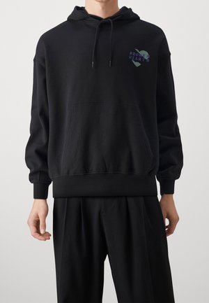 Sweatshirt noir avec capuche, poche avant et poignets côtelés. Présente le texte "BROKEN HEARTS" et un graphique de cœur en couleurs sur la poitrine.