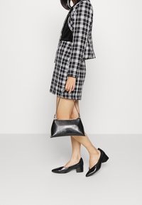 Rutig kavaj och kjolset i svart och vitt, ihop med platta, strukturerade svarta skor och en liten, glänsande svart handväska med dragkedja.