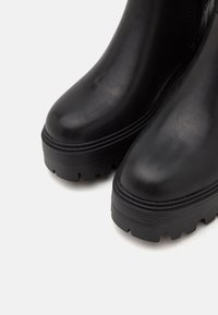 Bottes cheville en cuir noir avec un bout arrondi, une surface texturée et une semelle épaisse et robuste présentant des rainures pour l'adhérence.