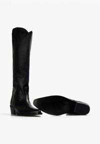 Botas de cuero negro hasta la rodilla con puntera afilada y un tacón bajo en bloque. El diseño presenta un acabado liso y un detalle mínimo.