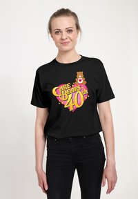 Camiseta de algodón negra con gráficos coloridos de un oso y texto que dice "Care Bears 40th" con un diseño de corazones y estrellas.