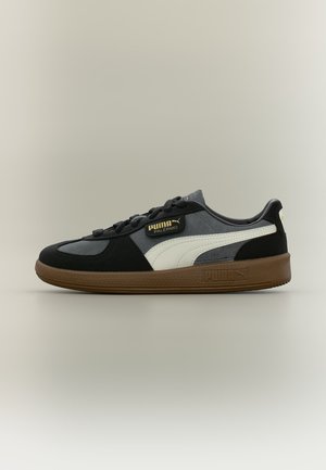 Zapatilla Puma Palermo de corte bajo en negro, gris y blanco con suela de goma y etiqueta lateral con la marca.