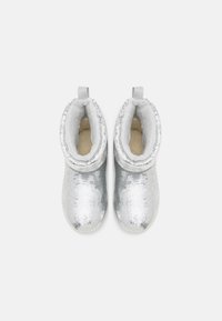 Paire de bottines argentées à sequins avec une doublure en polaire blanche et des languettes, présentées vue de dessus sur un fond clair uni.
