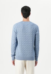 Pulover tricotat în nuanțe de albastru deschis, cu manșete și tiv cu dungi, având un model texturat. Proiectat cu un gât rotund și o siluetă ajustată.