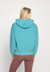 Sweatshirt de algodão azul-escuro com um grande capuz, punhos e cintura em malha. Usado com leggings castanhas. Design simples, textura suave.