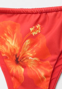 Rdeče bikini spodnje hlačke z velikim dizajnom hibiskusa v oranžni in rumeni barvi. Tekstura je gladka z elastičnimi robovi.