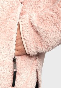 Futrzana różowa kurtka z zamkiem błyskawicznym z przodu i kieszenią boczną, charakteryzująca się miękką teksturą oraz czarnym uchwytem zamka, widocznymi szwami i podszewką.
