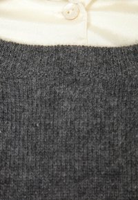 Šedý pletený svetr s texturovaným vzorem, pod nímž je vidět krémová saténová blůza s detaily knoflíčků.