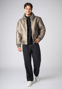 Leren bomberjack in gedempt grijs met een textuurafwerking, gecombineerd met een zachte, harige kraag. Gecombineerd met zwarte jeans en witte sneakers.
