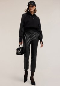 Felpa nera con cappuccio e cordoncino, abbinata a pantaloni in pelle a vita alta. Gli accessori includono una borsa nera con dettagli argentati e collant a fantasia.