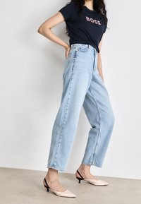 Jasnoniebieskie, wysokie dżinsy z prostymi nogawkami, połączone z granatowym T-shirtem z napisem "BOSS" w kwiatowym wzorze oraz jasnoróżowymi niskimi klapkami.