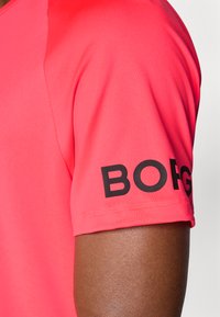 Short-sleeve, slim-fit shirt in bright pink fabric. Features a black "BORG" logo on the left sleeve. Smooth, lightweight texture.