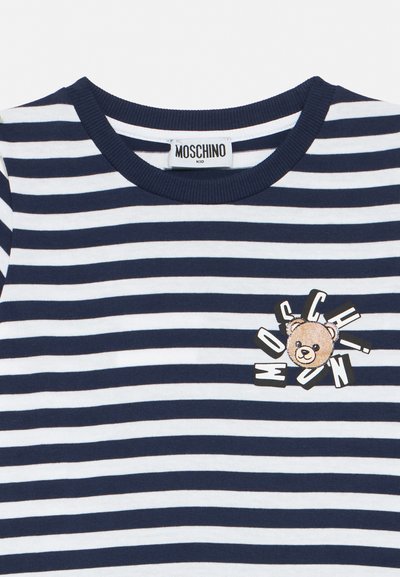 Μπλουζάκι με ναυτικές μπλε και λευκές ρίγες, λαιμόκοψη στρογγυλή, ετικέτα Moschino Kid και λογότυπο αρκουδάκι με διασκορπισμένο κείμενο της μάρκας στο στήθος.