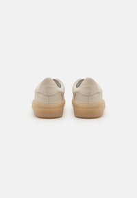 Beige lærersko med en myk tekstur, lav topp-design og gummisåler. Har et enkelt søm mønster og rund hæl.