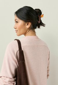 Ljusrosa tröja med en strukturerad yta, med en ribbad halsringning och ett brunt mockaband. Ett tortoiseshell-hårklipp håller håret i en bulle.