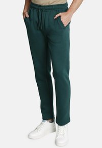 Sudadera verde oscuro con una cinturilla elástica, bolsillos laterales y un ajuste entallado, combinada con zapatillas blancas. Tejido de mezcla de algodón.