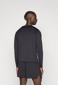 Hosszú ujjú fekete sportfelső könnyű anyagból, kerek nyakkivágással és karcsúsított szabással, hozzáillő rövidnadrággal párosítva.