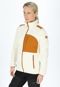 Fleece jacket, cream with brown accents. High collar, zippered chest pocket, and side pockets. Soft texture with a fitted design.