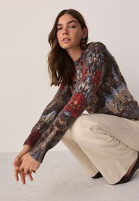 Džemper od pletenine s kombinacijom šarenih cvjetnih i apstraktnih uzoraka u smeđim, crvenim, plavim i žutim tonovima, s rebrastim manžetnama i okruglim izrezom.