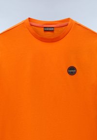 Kortærmet orange t-shirt lavet af bomuld, med rund halsudskæring og et lille rundt logo-patch på venstre bryst.